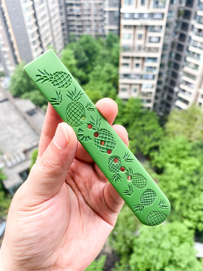 May include: A green watch strap with a pineapple pattern. The strap is made of a soft, flexible material and has a textured surface.