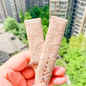 May include: Two light pink silicone watch bands with a floral pattern. The bands have a delicate floral design with a light brown color.