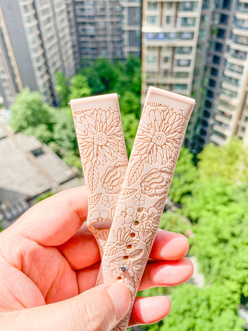 May include: Two light pink silicone watch bands with a floral pattern. The bands have a delicate floral design with a light brown color.