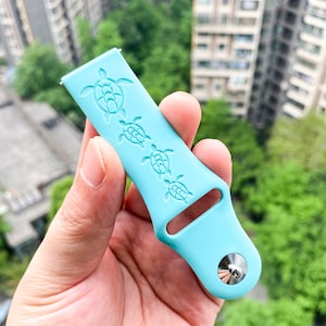 Puede incluir: Una correa de reloj de silicona azul claro con un dise&ntilde;o de cuatro tortugas marinas. La correa tiene una hebilla de metal plateado.