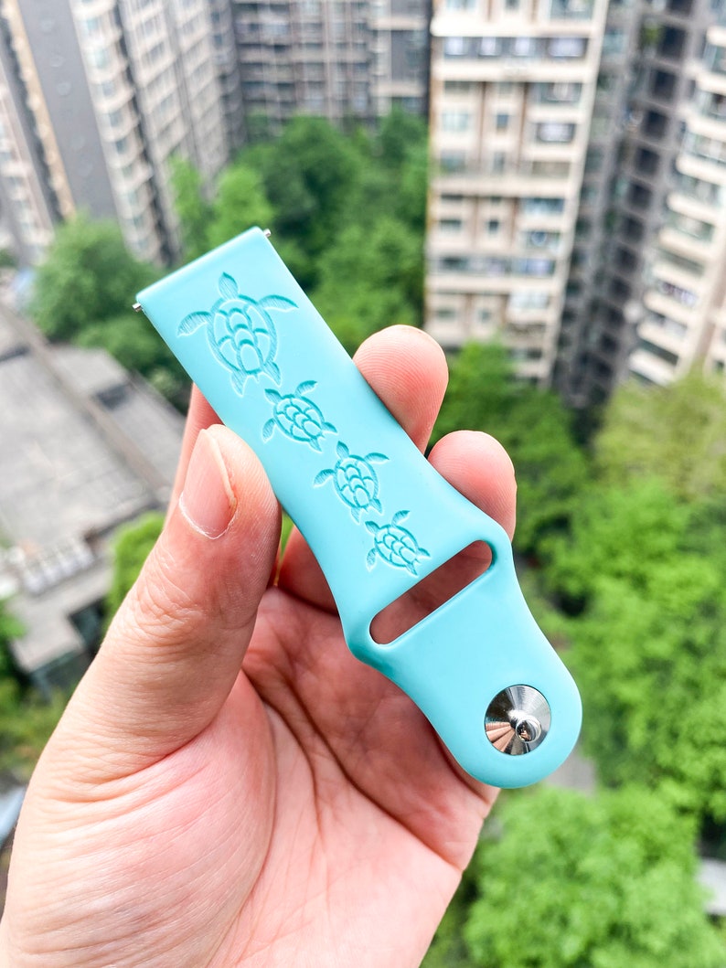 Puede incluir: Una correa de reloj de silicona azul claro con un dise&ntilde;o de cuatro tortugas marinas. La correa tiene una hebilla de metal plateado.