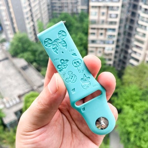 May include: A light blue silicone watch band with a Mickey Mouse design. The band has a silver buckle and is decorated with various Mickey Mouse characters and icons.
