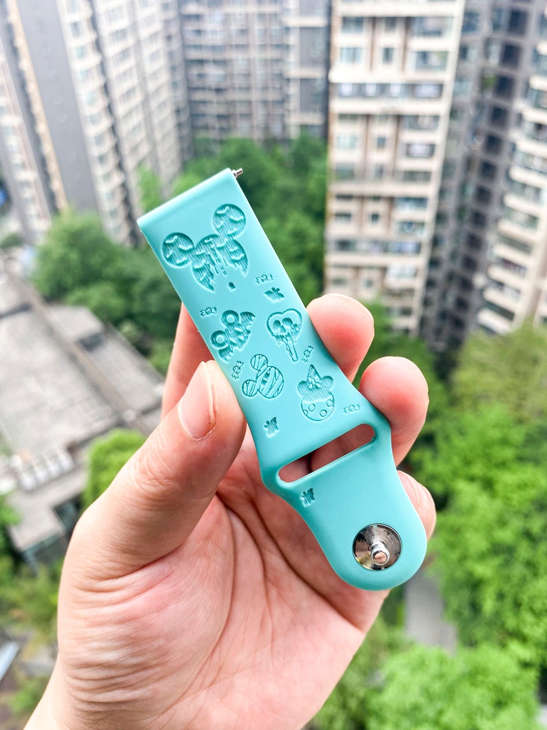 May include: A light blue silicone watch band with a Mickey Mouse design. The band has a silver buckle and is decorated with various Mickey Mouse characters and icons.