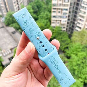 May include: A light blue silicone watch band with a Winnie the Pooh design. The band features a repeating pattern of honey pots, bees, and Winnie the Pooh holding balloons.