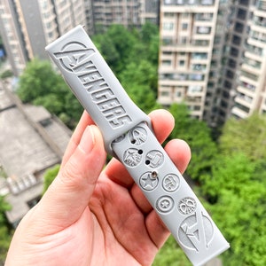 May include: A gray watch band with the word "Avengers" and various superhero logos embossed on it.