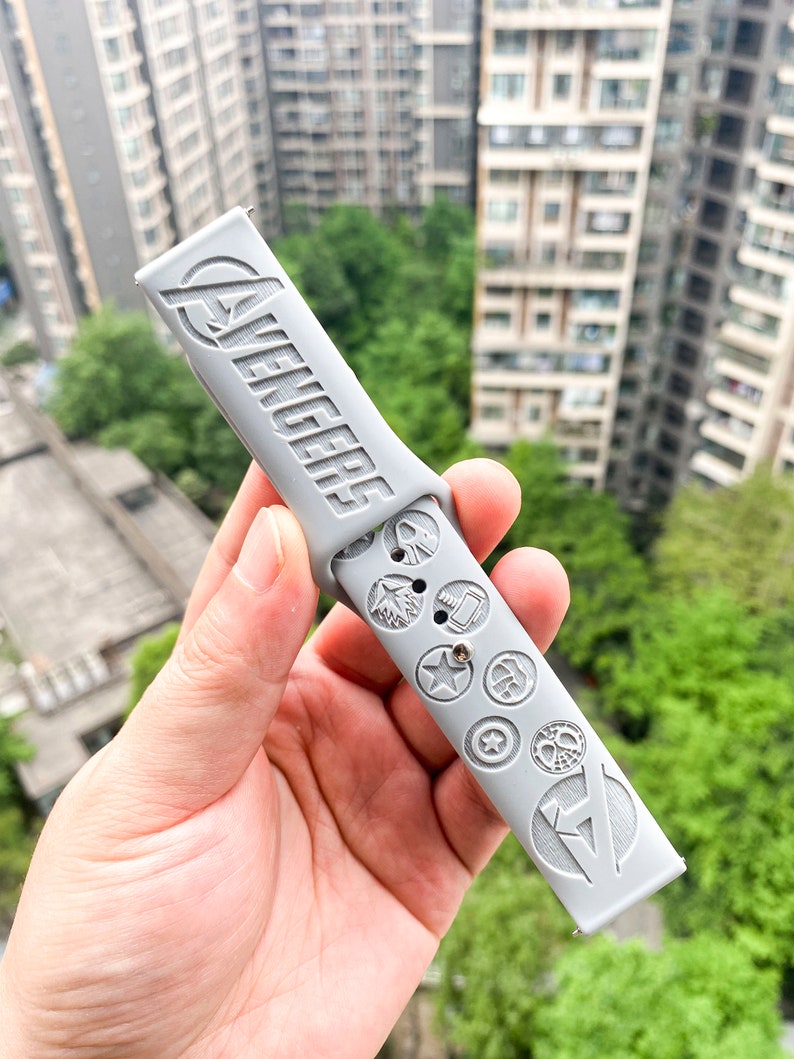May include: A gray watch band with the word "Avengers" and various superhero logos embossed on it.