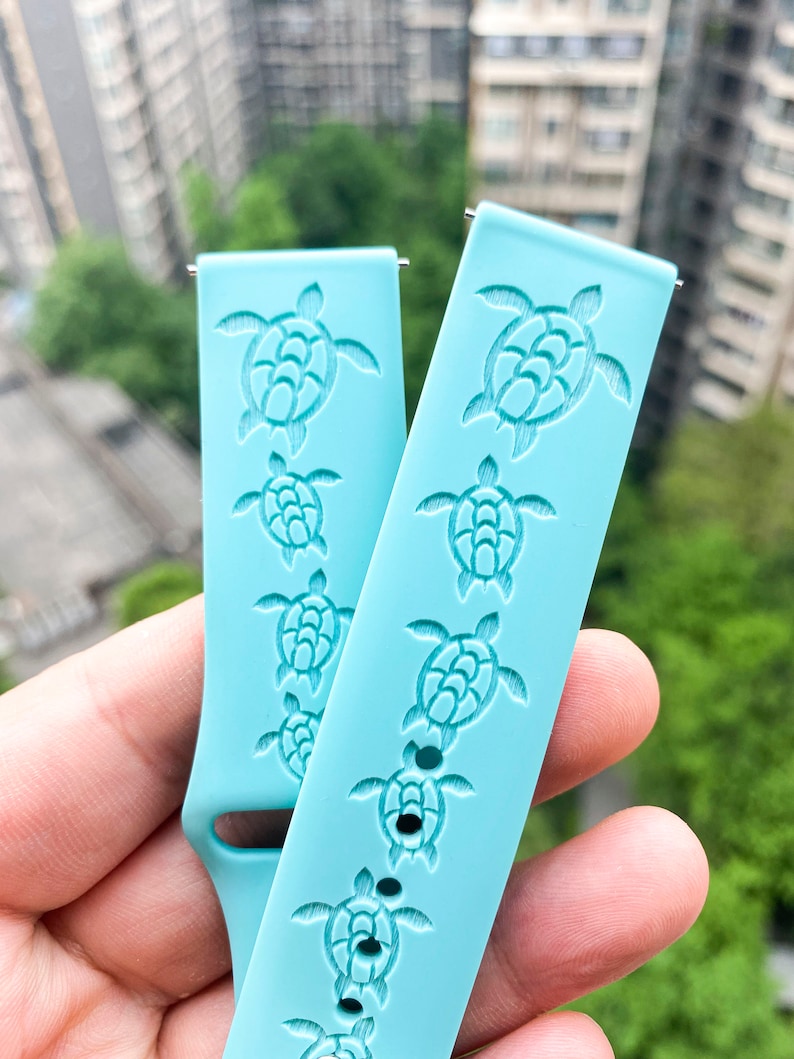 Puede incluir: Dos correas de reloj de silicona azul claro con un patr&oacute;n repetido de tortugas marinas. Las tortugas est&aacute;n en relieve en las correas.