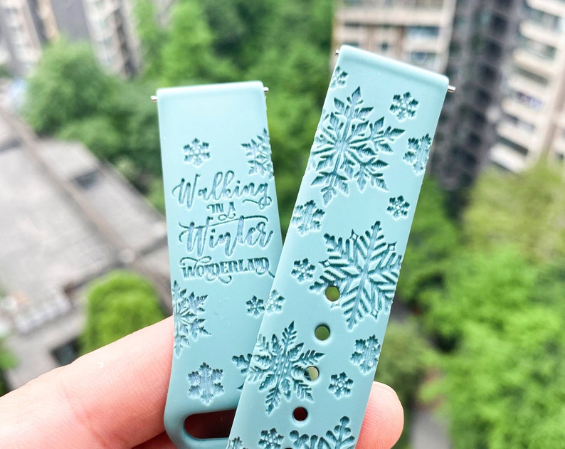 Op de afbeelding: Twee lichtblauwe horlogebandjes met een sneeuwvlokkenpatroon. Een bandje heeft de tekst "Walking in a Winter Wonderland" erop gedrukt.