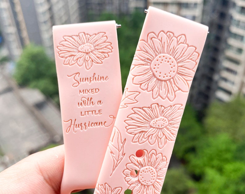 Op de afbeelding: Twee roze siliconen horlogebandjes met een bloemenpatroon en reli&euml;ftekst. De tekst op een bandje luidt "Sunshine mixed with a little Hurricane".