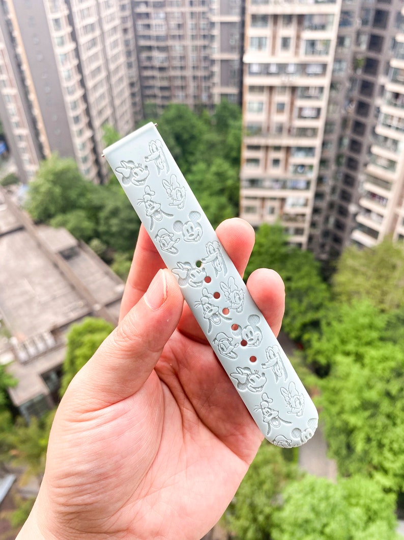 May include: A light blue silicone watch strap with a repeating pattern of Mickey Mouse and Minnie Mouse characters.
