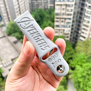 May include: A gray silicone watch band with the word "Avengers" embossed on it. The band has a silver metal buckle with various superhero symbols embossed on it.
