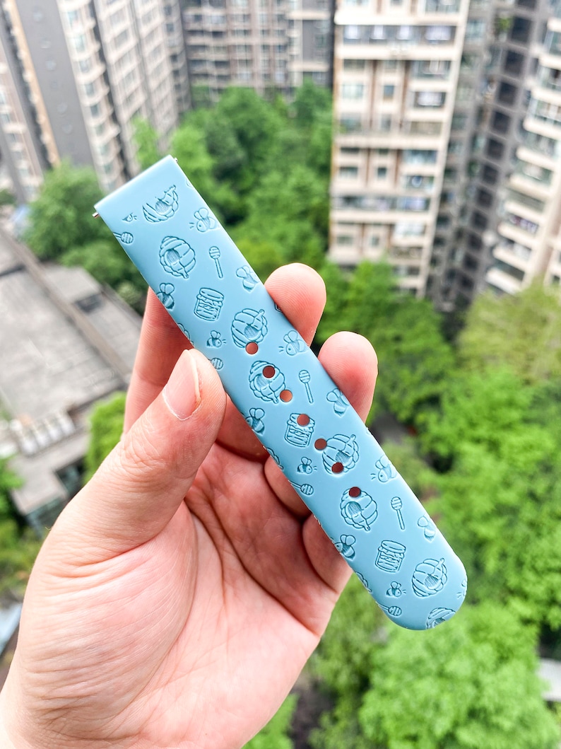 May include: A light blue silicone watch band with a repeating pattern of honeycombs, bees, and honey jars.