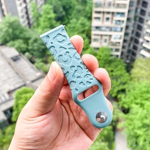 May include: A light blue silicone watch band with a leopard print design. The band has a silver buckle.