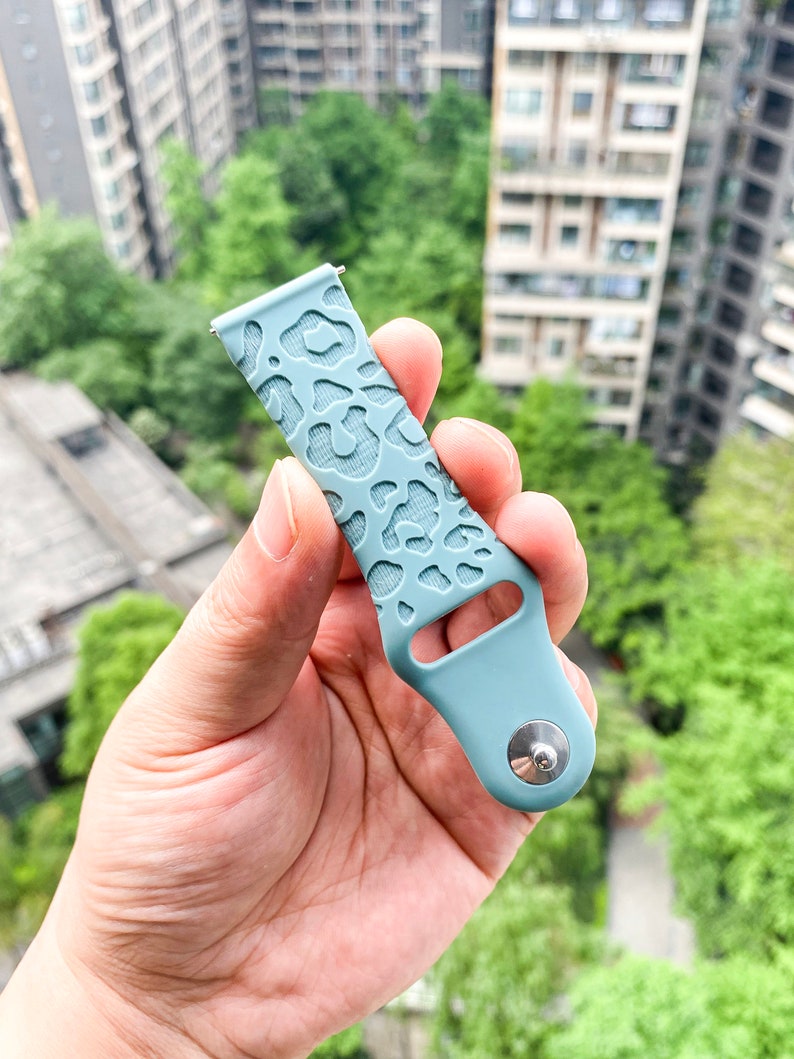 May include: A light blue silicone watch band with a leopard print design. The band has a silver buckle.