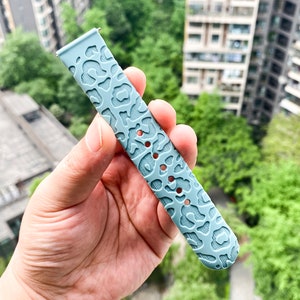 May include: A light blue silicone watch band with a leopard print design.