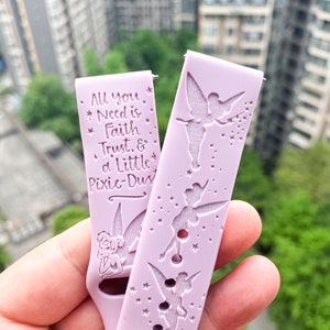 May include: A pink silicone watch band with a Tinkerbell design. The band features a quote: "All you need is faith, trust, & a little pixie dust".