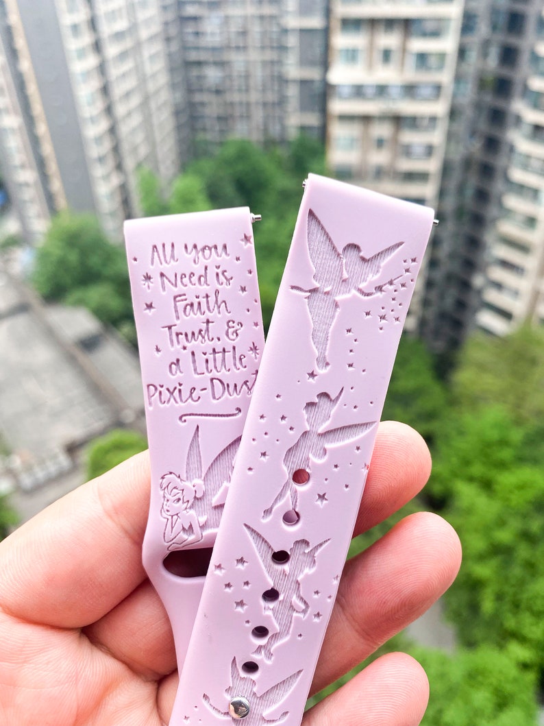 May include: A pink silicone watch band with a Tinkerbell design. The band features a quote: "All you need is faith, trust, & a little pixie dust".
