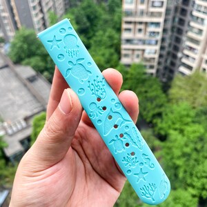 以下が含まれることがあります： 海の生き物のデザインが施された薄い青色の腕時計のバンド。バンドには、ヒトデ、クラゲ、タツノオトシゴ、カメ、サンゴが描かれています。