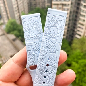 May include: Two light blue silicone watch bands with a floral pattern. The bands are embossed with a delicate floral design.