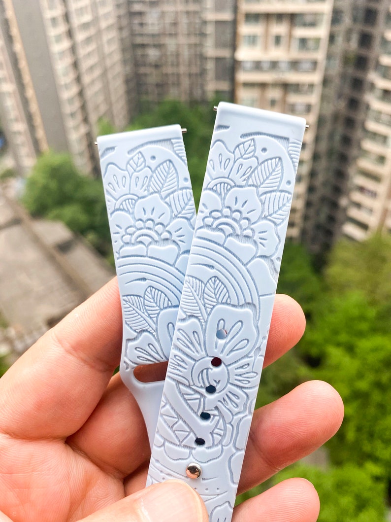 May include: Two light blue silicone watch bands with a floral pattern. The bands are embossed with a delicate floral design.