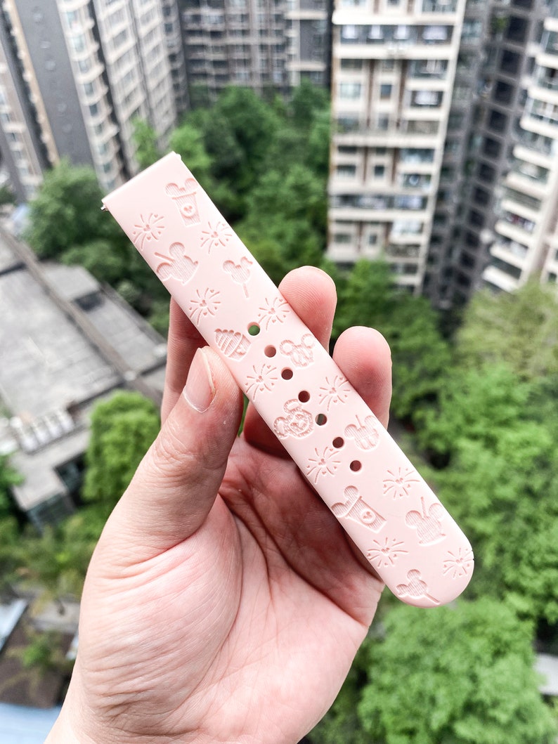 May include: A pink silicone watch band with a repeating pattern of Mickey Mouse, fireworks, and other Disney-themed icons.