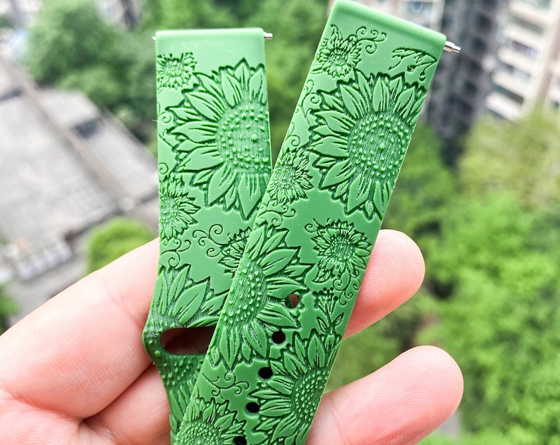 May include: Two green silicone watch bands with a sunflower pattern. The bands are embossed with a detailed sunflower design.