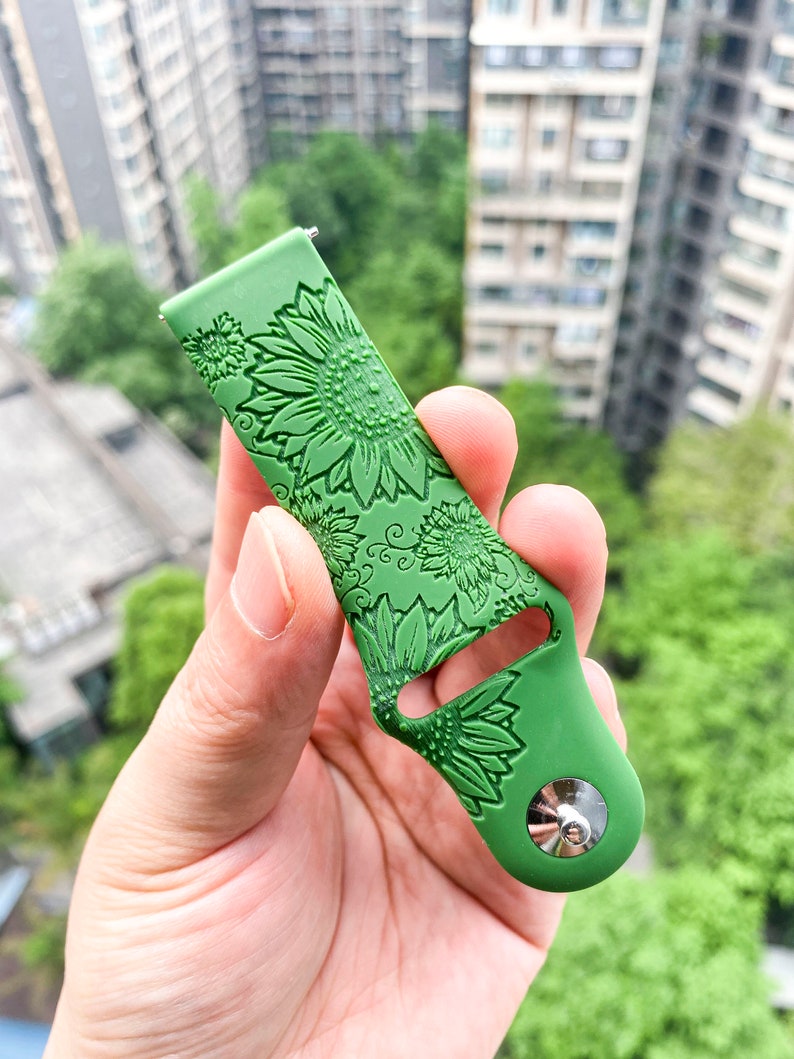 May include: Green silicone watch band with a sunflower pattern embossed on the surface. The band has a silver metal buckle.