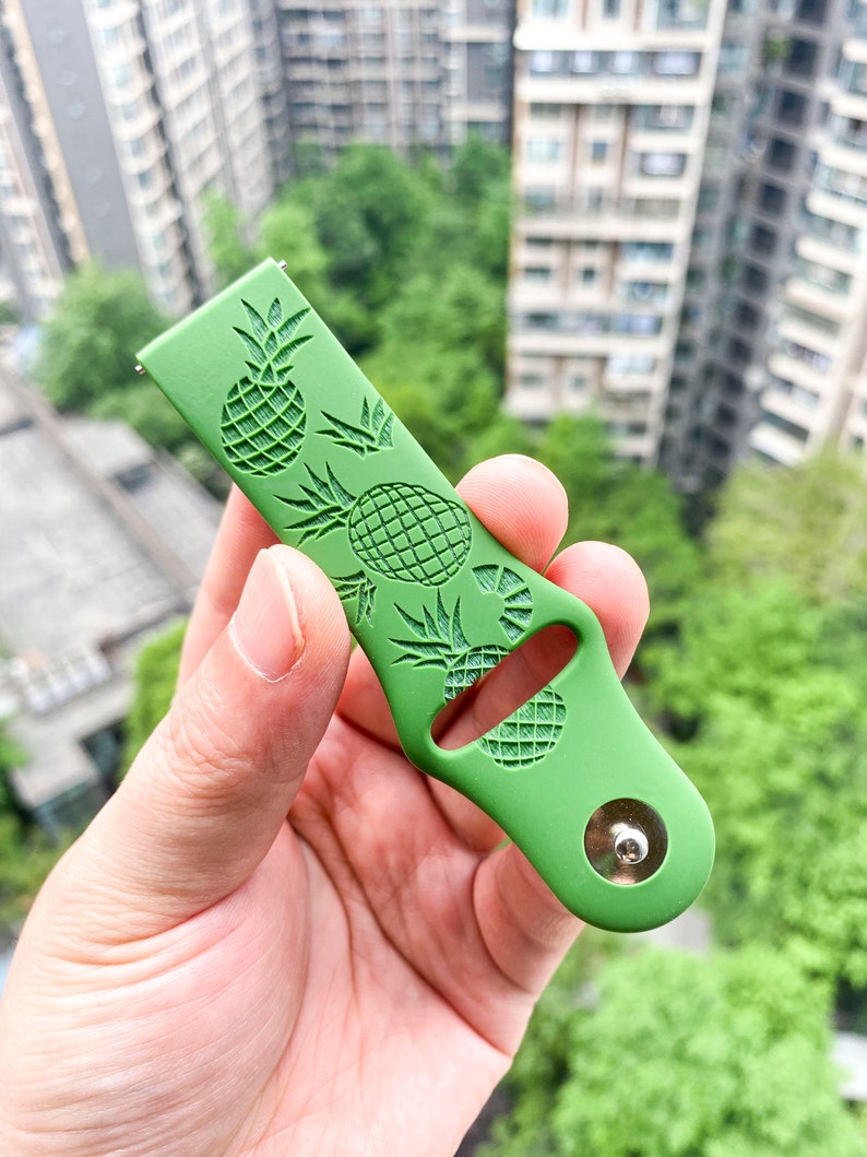 May include: Green silicone watch strap with a pineapple pattern. The strap has a silver metal buckle.
