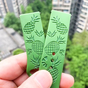 May include: Two green watch straps featuring a pineapple design. The straps are made from a soft, flexible material and have a textured finish.