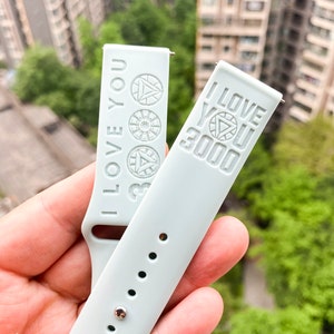 May include: Two light blue silicone watch bands with the words "I Love You 3000" embossed on them. The bands have a silver metal buckle and are designed for a smartwatch.