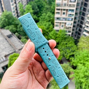 Puede incluir: Una correa de reloj de silicona azul claro con un patr&oacute;n de cactus y corazones.