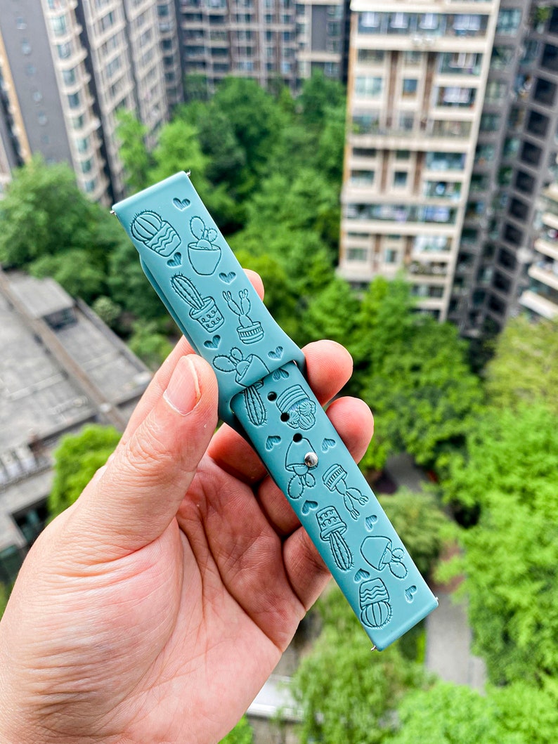 Puede incluir: Una correa de reloj de silicona azul claro con un patr&oacute;n de cactus y corazones.