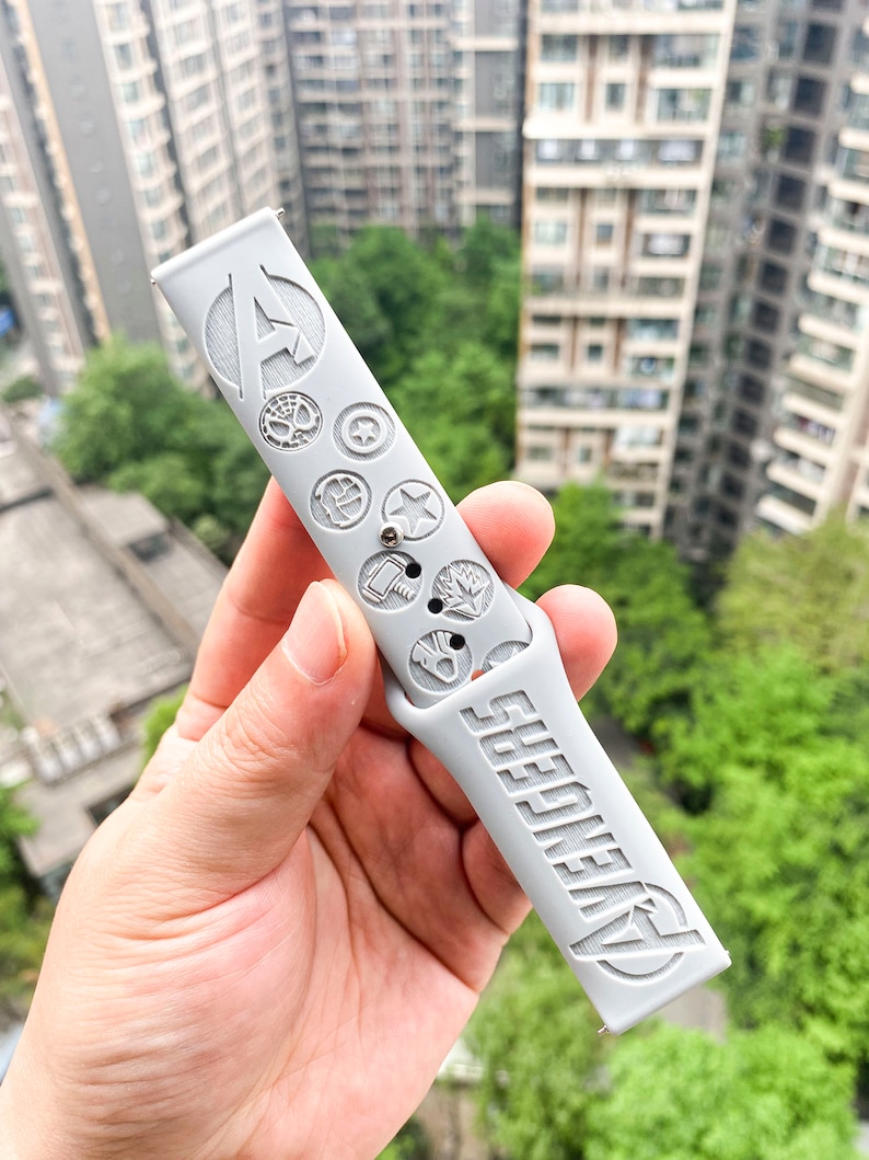 May include: Gray silicone watch band with the Avengers logo and various Marvel character symbols embossed on the band.