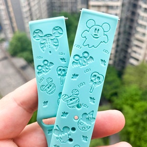 May include: Two turquoise blue silicone watch bands with a Halloween theme. The bands feature Mickey Mouse, ghosts, bats, and candy corn.