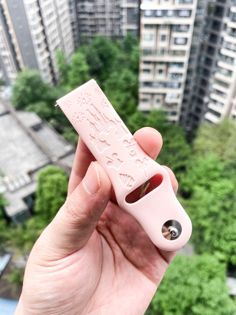 May include: A pink silicone watch band with a white embossed design of Cinderella's castle and other Disney characters.