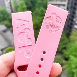 May include: Two pink silicone watch bands. One band has the text "PASSHOLDER" and a Mickey Mouse silhouette. The other band has the text "A&P" and a Mickey Mouse silhouette.