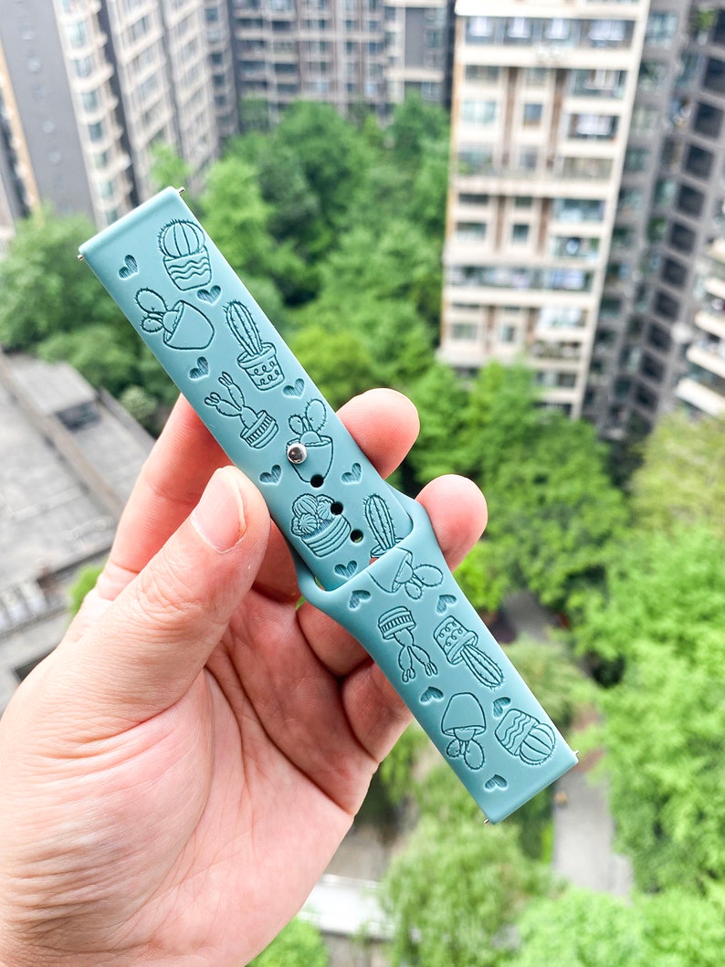 Puede incluir: Una correa de reloj de silicona azul claro con un dise&ntilde;o de cactus y plantas.