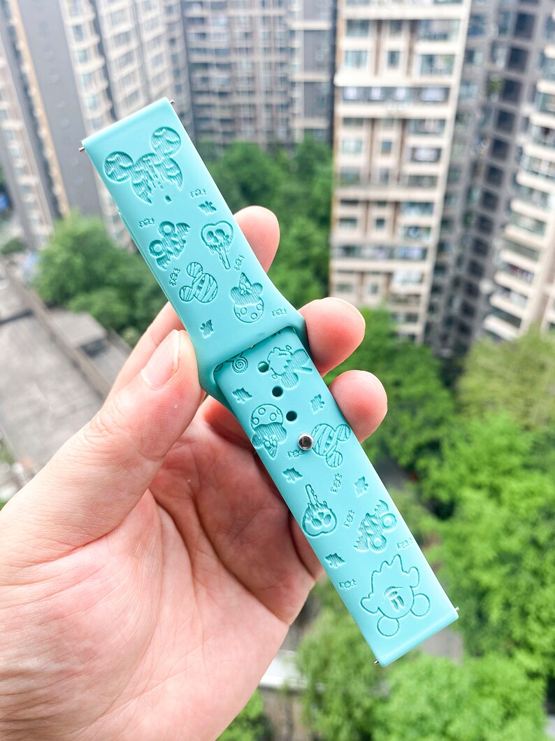 May include: A light blue silicone watch band with a repeating pattern of cartoon characters and designs. The band has a silver metal connector on one end.