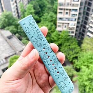 Puede incluir: Una correa de reloj de silicona azul claro con un patr&oacute;n de cactus y corazones.