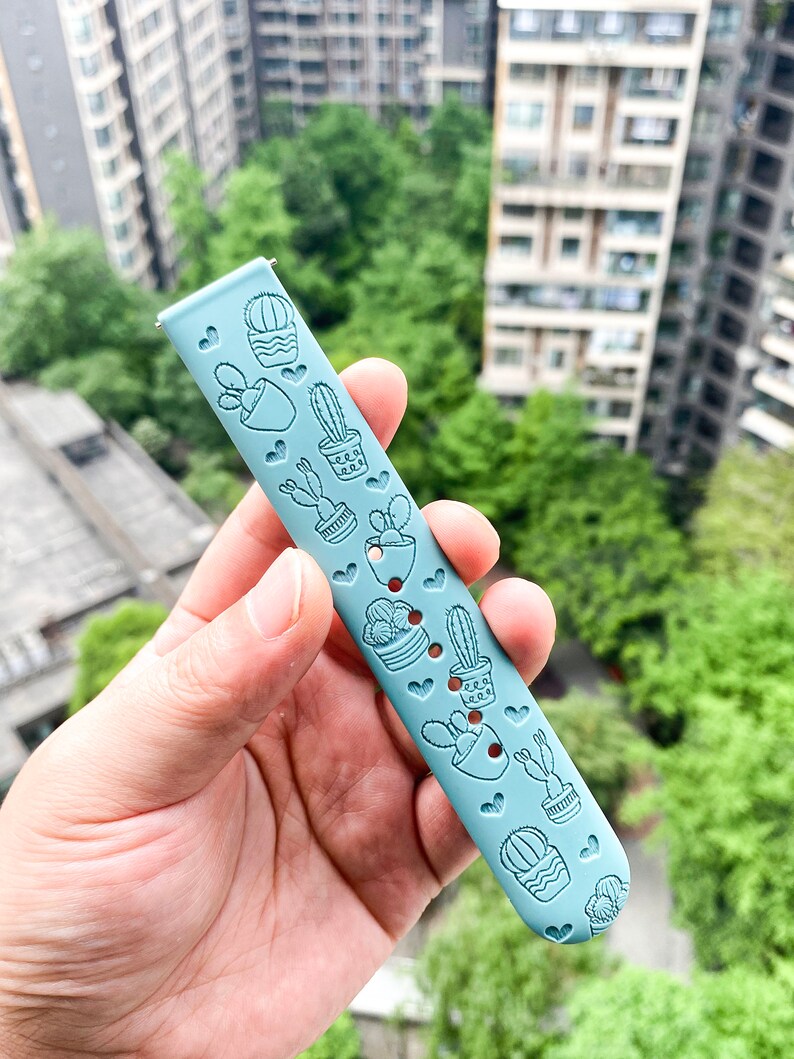 Puede incluir: Una correa de reloj de silicona azul claro con un patr&oacute;n de cactus y corazones.