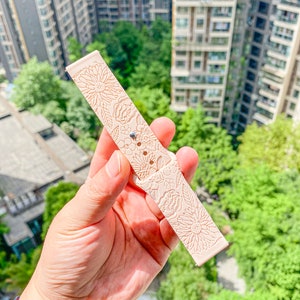 May include: A pale pink watch band with a floral pattern. The band is made of a soft, flexible material and has a smooth finish.