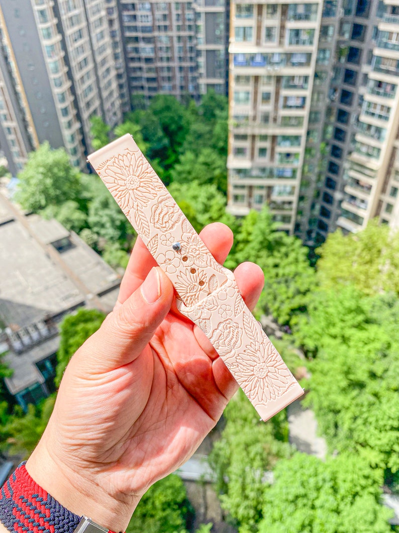 May include: A pale pink watch band with a floral pattern. The band is made of a soft, flexible material and has a smooth finish.
