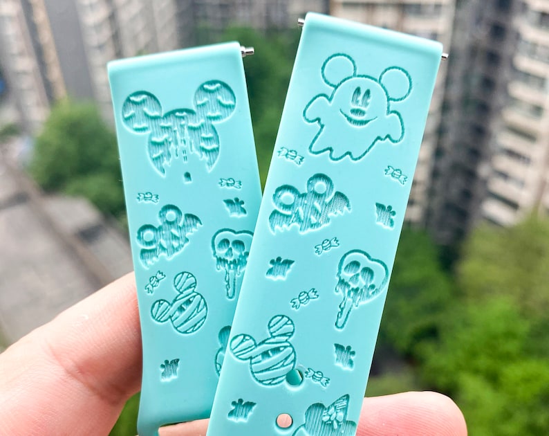 May include: Two light blue silicone watch bands with Halloween themed designs. One band features a ghost with Mickey Mouse ears and the other band features a variety of Halloween icons including Mickey Mouse ears, bats, and candy.