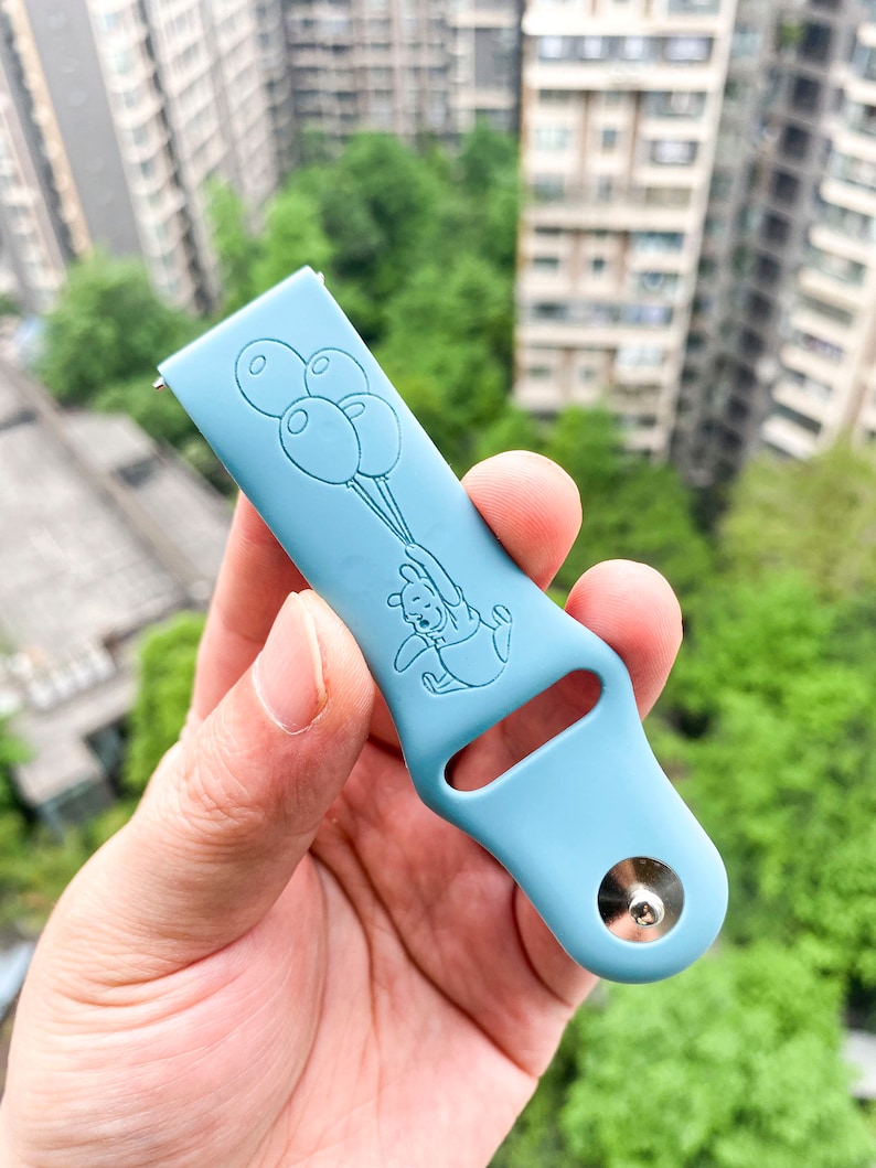 May include: A light blue silicone watch band with a Winnie the Pooh design. Pooh is holding balloons and the band has a silver metal buckle.
