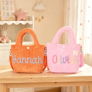 May include: Two corduroy tote bags with handles and detachable shoulder straps. The orange bag features the name Hannah in light blue script, and the pink bag features the name Olivia in multicolored script with a small white flower applique.