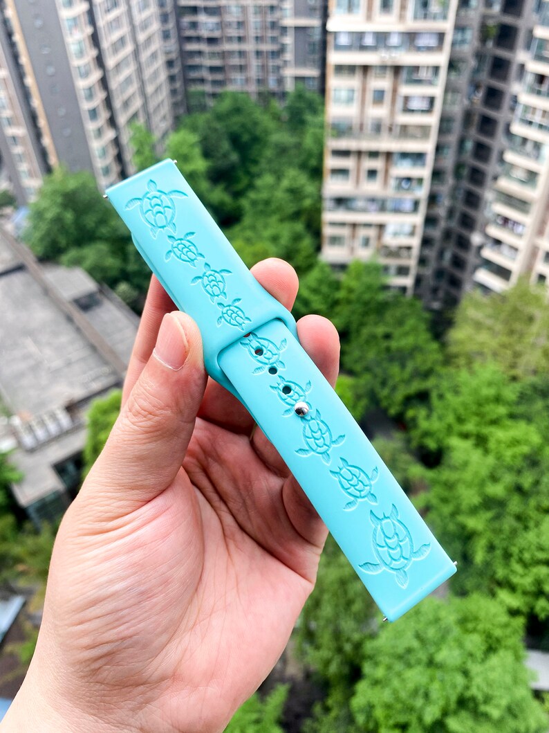 Puede incluir: Una correa de reloj de silicona azul claro con un patr&oacute;n repetido de tortugas marinas en relieve en la superficie.