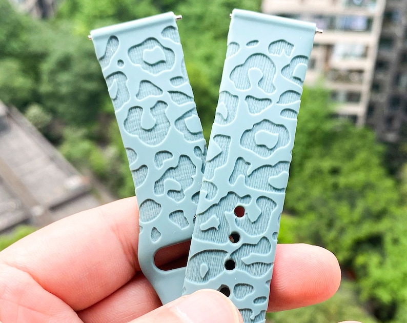 May include: Two light blue watch bands with a leopard print design. The bands are made of a soft, flexible material and have a smooth finish.
