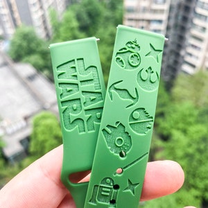 May include: Green silicone watch strap with a Star Wars theme. The strap features the words "Star Wars" and various Star Wars characters, including R2-D2, a lightsaber, and the Death Star.