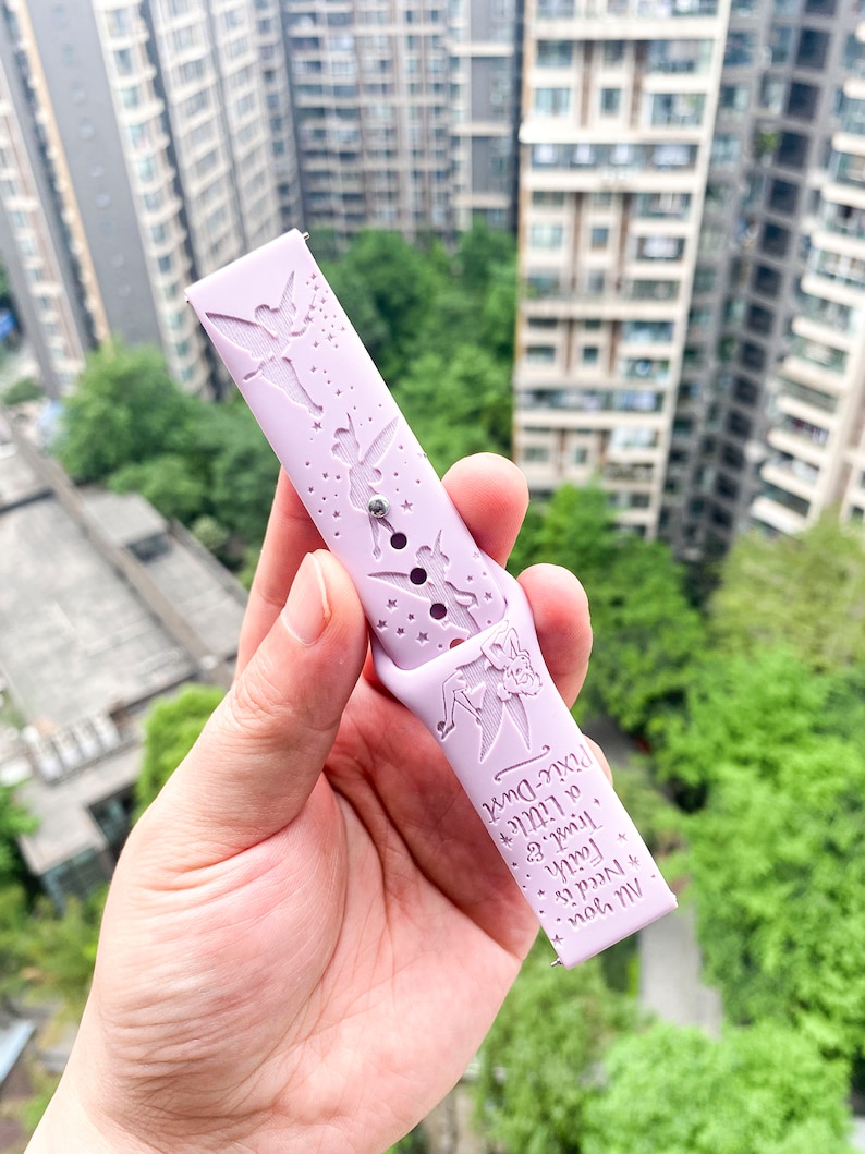 May include: A light purple silicone watch band with a Tinkerbell design. The band features a silhouette of Tinkerbell flying with stars and the text "All you need is faith, trust, and a little bit of pixie dust".