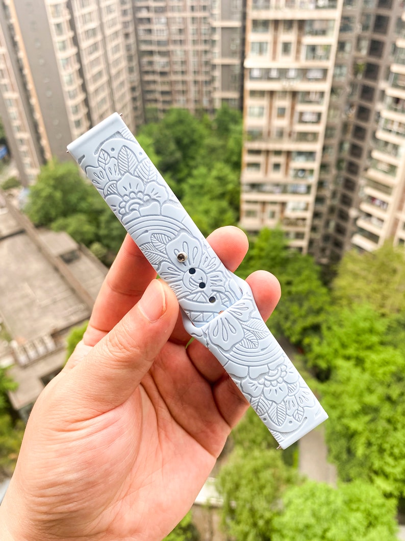May include: A light blue silicone watch band with a floral pattern. The band is embossed with a delicate floral design.